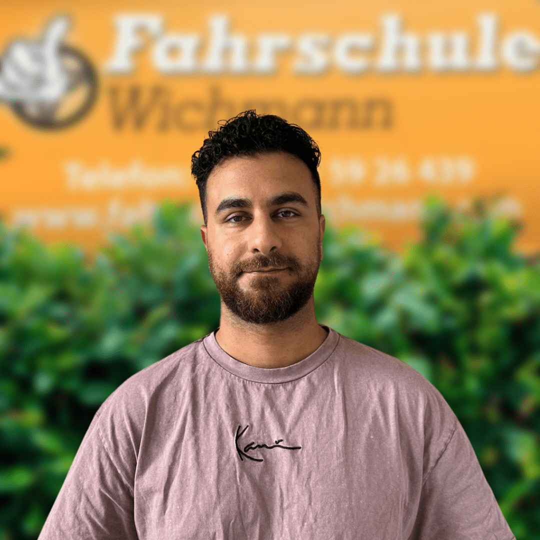 Azidin ist Fahrlehrer bei der Fahrschule Wichmann in Delmenhorst – dein Ansprechpartner für Autoführerschein, Motorradführerschein, LKW Führerschein, Anhängerführerschein, Intensivfahrschule und Fahrlehrerausbildung. - Fahrschule Wichmann Delmenhorst - Autoführerschein LKW Führerschein Motorradführerschein Azidin, Fahrlehrer der Fahrschule Wichmann in Delmenhorst, vor dem gelben Firmenschild mit Logo und Kontaktdaten.