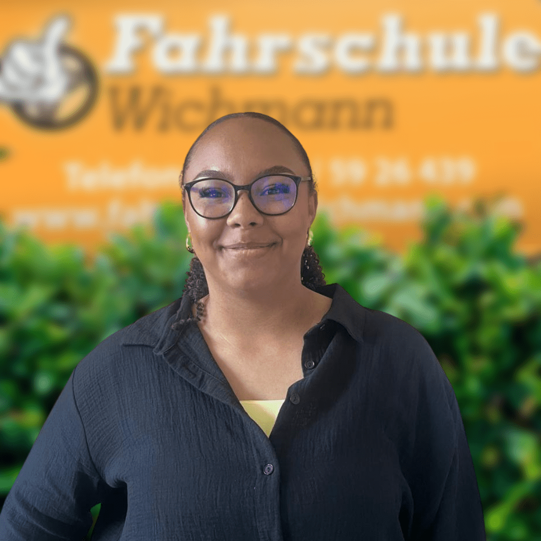 Charline, Fahrlehrerin der Fahrschule Wichmann in Delmenhorst, bietet Ausbildung für Autoführerschein, Motorradführerschein, LKW Führerschein, Anhängerführerschein sowie Intensivfahrschule und Fahrlehrerausbildung mit Herz und Kompetenz. - Fahrschule Wichmann Delmenhorst - Autoführerschein LKW Führerschein Motorradführerschein Charline, Fahrlehrerin der Fahrschule Wichmann in Delmenhorst, vor dem gelben Logo mit grüner Hecke.