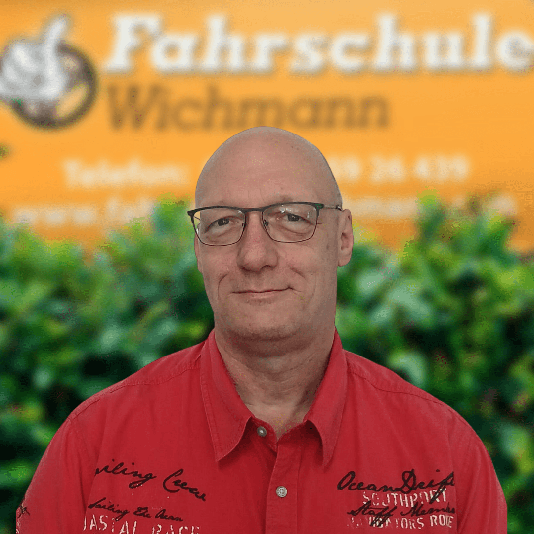 Hans-Peter, Fahrlehrer der Fahrschule Wichmann in Delmenhorst, bereitet dich kompetent auf den Auto-, Motorrad-, LKW- und Anhängerführerschein vor – auch als Intensivfahrschule oder Fahrlehrerausbildung. - Fahrschule Wichmann Delmenhorst - Autoführerschein LKW Führerschein Motorradführerschein Hans-Peter, Fahrlehrer der Fahrschule Wichmann Delmenhorst, steht vor dem Logo der Fahrschule im roten Hemd.