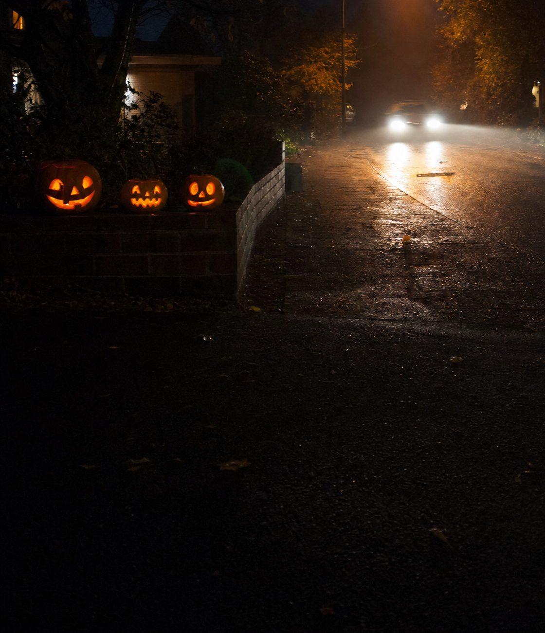 Halloween-Nacht: leuchtende Kürbisse an einer nebligen Straße